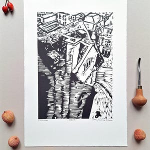 The photo shows a linocut - a birds-eye view from the Carfax tower in Oxford, England. The print is placed on a grey background. To its right is a Pfeil gouge, a tool for carving linocuts. There are some  litchi fruit around the print and a rosehip.