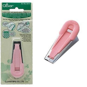 May include: Pink plastic and metal bias tape maker with a clear plastic window. The tool is labeled "Clover" and "Art No. 4014".