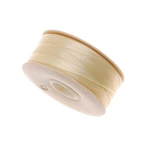May include: A spool of cream-colored thread wound around a cardboard bobbin.