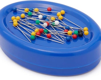 May include: A blue magnetic pin holder filled with sewing pins. The pins have colorful heads in red, yellow, green, blue, white, and black. The pins are scattered across the oval-shaped holder, ready for use in sewing projects.