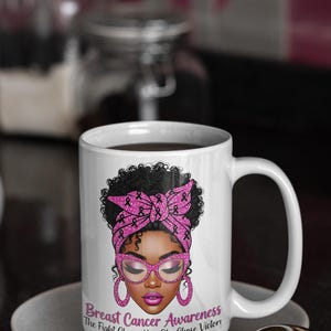May include: White ceramic mug featuring a woman with a pink headscarf and glasses, designed for breast cancer awareness. The mug includes the text "Breast Cancer Awareness The Fight Chose Her. She Chose Victory!" on the front. The mug is on a white saucer.