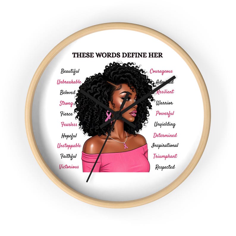 May include: A round wall clock with a light wood frame. The clock face features an illustration of a woman with curly black hair and pink accents. Text around the image reads "THESE WORDS DEFINE HER" and lists empowering words.