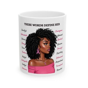 May include: White ceramic mug featuring a portrait of a woman with curly black hair, wearing a pink top and earrings. The mug has the text "THESE WORDS DEFINE HER" and a list of empowering words in pink.