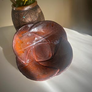 May include: A brown ceramic bowl with a unique, folded design. The bowl has a speckled, glittery finish and is perfect for serving snacks or holding small items.
