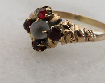 May include: A gold ring with a white stone surrounded by five red gemstones.