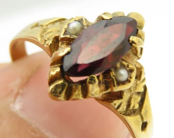 May include: A gold ring with a maroon marquise-shaped gemstone surrounded by two small white pearls.