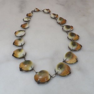 May include: A necklace made of brown, white, and green shell beads with silver metal clasps.