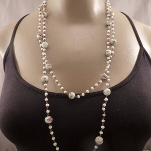 May include: A long white beaded necklace with small white beads and larger white beads with brown and white patterns.