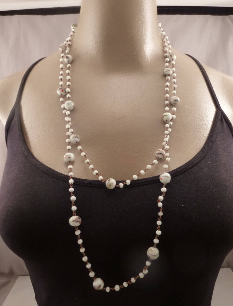 May include: A long white beaded necklace with small white beads and larger white beads with brown and white patterns.