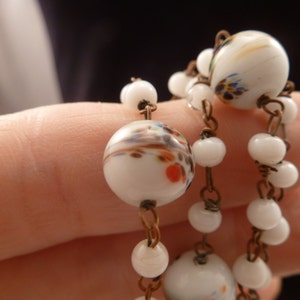 May include: A white glass beaded necklace with a brown wire chain. The beads are decorated with colorful floral patterns.