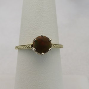May include: A gold ring featuring a large, round, dark brown gemstone. The ring has a detailed band with a repeating pattern. The gemstone is held in place by six prongs.