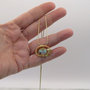 May include: A gold necklace with a pendant featuring a pink and gold oval-shaped stone surrounded by a gold snake design.