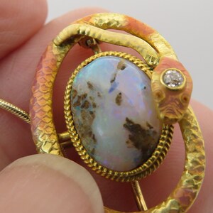 May include: A gold snake brooch with a large opal gemstone and a small diamond accent. The snake is coiled around the opal, and the diamond is set in the snake's head.