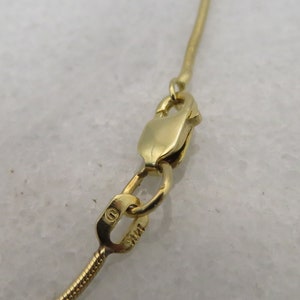 May include: Close-up of a gold chain necklace clasp with a small circular hallmark that reads "14K".