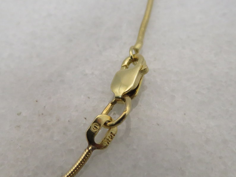 May include: Close-up of a gold chain necklace clasp with a small circular hallmark that reads "14K".