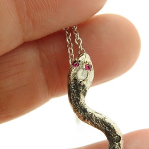 May include: Silver snake pendant necklace with ruby eyes and a diamond on the head. The snake is curled in a realistic pose.