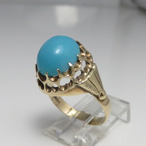 May include: A gold ring with a large, round, turquoise stone set in a decorative, openwork setting.
