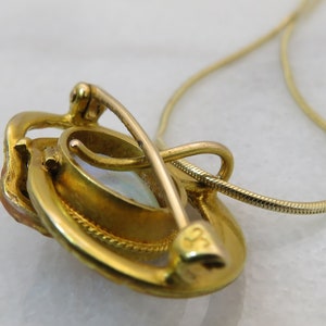 May include: A gold pendant necklace with a white opal stone set in a gold frame. The pendant has a clasp on the back and is attached to a delicate gold chain.