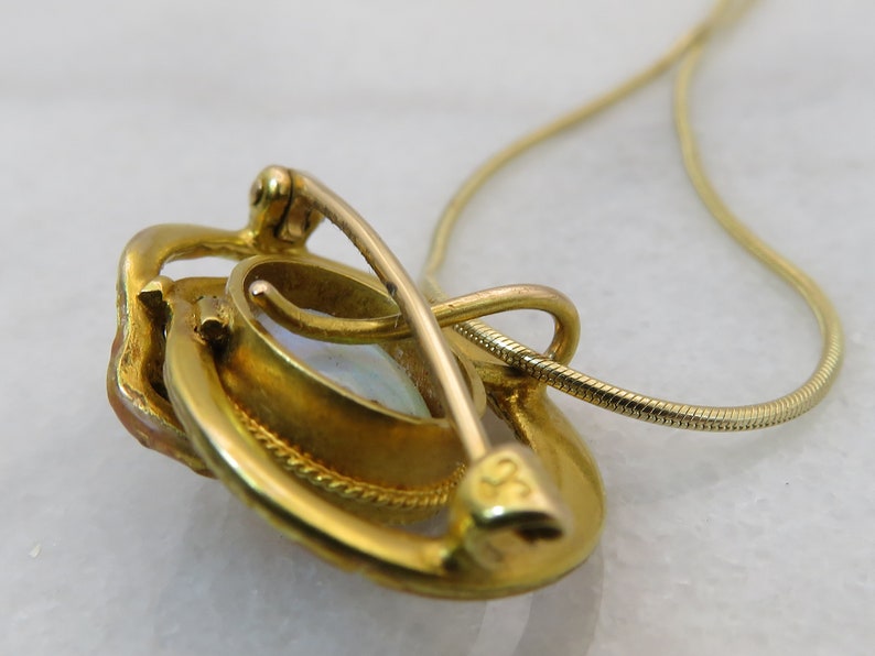 May include: A gold pendant necklace with a white opal stone set in a gold frame. The pendant has a clasp on the back and is attached to a delicate gold chain.