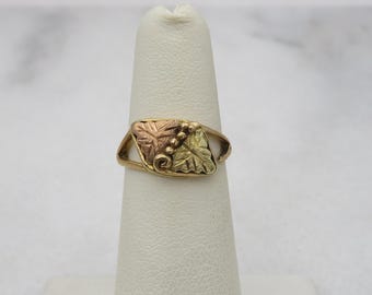 May include: A gold ring featuring a three-toned leaf design. The leaves are green, yellow, and rose gold.