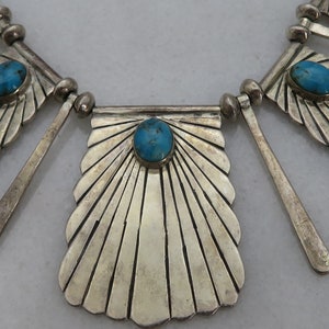 May include: A silver necklace with turquoise stones and a fan-shaped design. The necklace is made of sterling silver and features a unique geometric pattern.