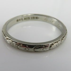 May include: A silver wedding band with a floral design and the inscription "BELAIS 18K".