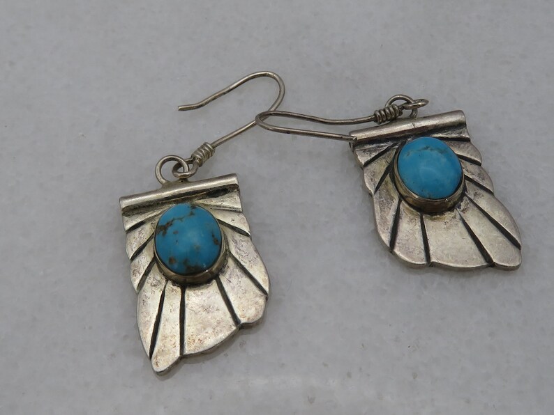 May include: A pair of silver earrings with turquoise stones set in a fan-shaped design.