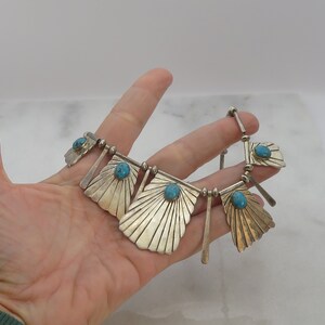 May include: A silver necklace with turquoise stones and a fan-shaped design. The necklace is made of sterling silver and features five turquoise stones.