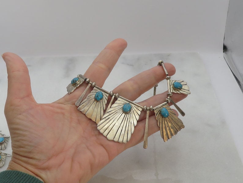 May include: A silver necklace with turquoise stones and a fan-shaped design. The necklace is made of sterling silver and features five turquoise stones.