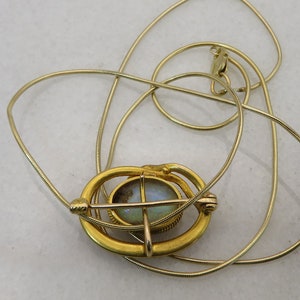 May include: A gold chain necklace with a pendant featuring a round opal stone set in a gold frame. The frame has a delicate design with a cross shape.