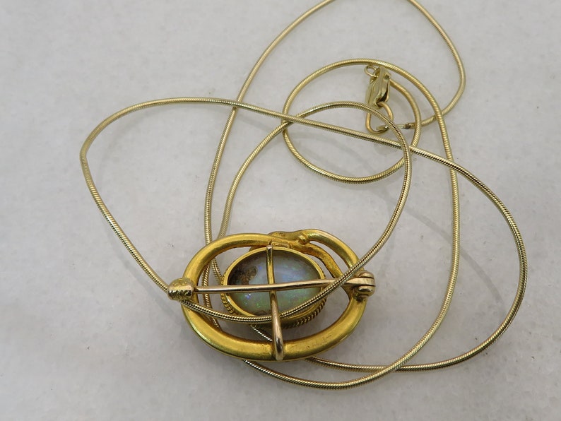 May include: A gold chain necklace with a pendant featuring a round opal stone set in a gold frame. The frame has a delicate design with a cross shape.