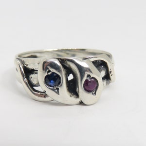 May include: A silver ring with a twisted snake design. The ring has two gemstones, one blue and one red.