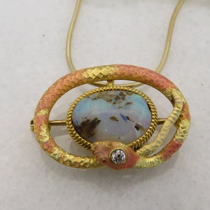 May include: A gold snake pendant necklace with a large opal gemstone and a small diamond accent. The snake is coiled around the opal and has a textured, enamel-like finish.