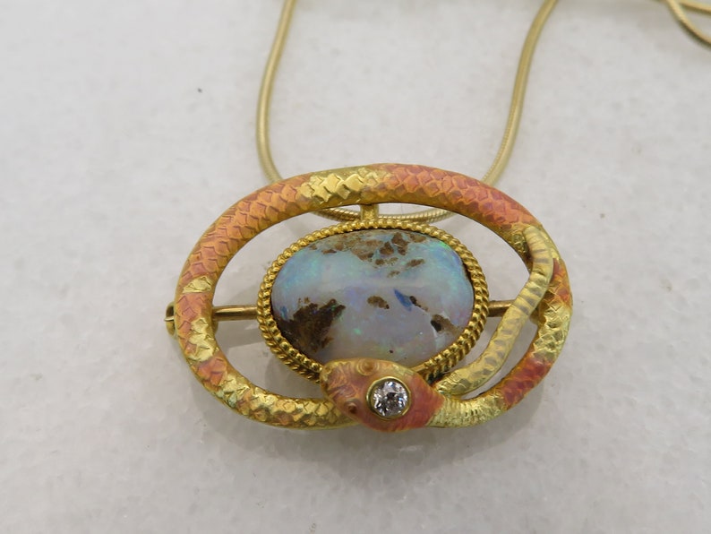 May include: A gold snake pendant necklace with a large opal gemstone and a small diamond accent. The snake is coiled around the opal and has a textured, enamel-like finish.