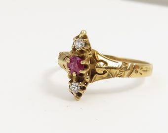 May include: A gold ring with a red ruby and two white diamonds set in a delicate, ornate design.
