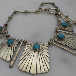 May include: A silver necklace with turquoise stones and a fan-shaped design. The necklace is made of sterling silver and features a unique geometric pattern.