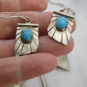 May include: A pair of silver earrings with turquoise stones. The earrings are in the shape of a leaf with a scalloped edge.