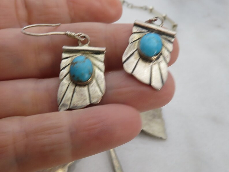 May include: A pair of silver earrings with turquoise stones. The earrings are in the shape of a leaf with a scalloped edge.