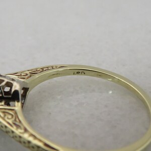 May include: Close-up of a gold ring with a filigree design and a gemstone setting. The ring is marked "14k" on the band. The ring's intricate details and warm gold color are highlighted.