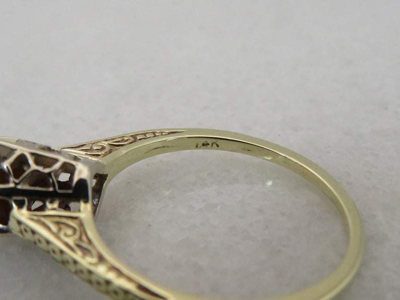 May include: Close-up of a gold ring with a filigree design and a gemstone setting. The ring is marked "14k" on the band. The ring's intricate details and warm gold color are highlighted.