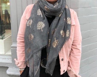May include: A woman wearing a pink corduroy jacket over a black dress with a gray scarf with gold tree designs.