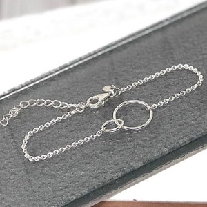 May include: A silver chain bracelet with two interlocking circles. The bracelet has a lobster clasp closure.