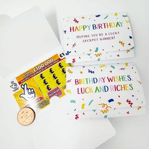 Könnte beinhalten: Weiße Geburtstagskarte mit bunten Konfetti und dem Text "HAPPY BIRTHDAY HOPING YOU'RE A LUCKY JACKPOT WINNER!". Ein Lotterieschein und eine Münze sind in einem weißen Umschlag zu sehen.
