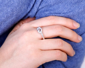 Op de afbeelding: Een zilveren knoop ring met een gladde, gepolijste afwerking. De ring wordt gedragen aan de wijsvinger van een hand.