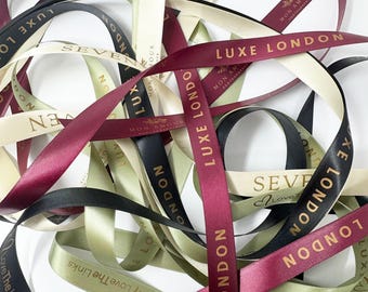 May include: Assortment of satin ribbons in various colors, including burgundy, black, and cream. The ribbons are printed with gold text, featuring phrases like "LUXE LONDON" and "Love The Links". Ideal for gift wrapping or crafting.