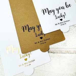 May include: Three white cards with gold and black lettering. The cards have the text "May you be Lucky!" with a heart symbol and the text "Mr & Mrs Dalton 19.06.24".