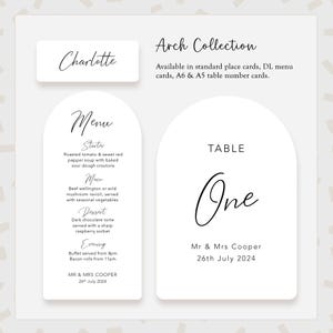May include: White arch-shaped table number card with the text "TABLE One" and the names "Mr & Mrs Cooper" and the date "26th July 2024".