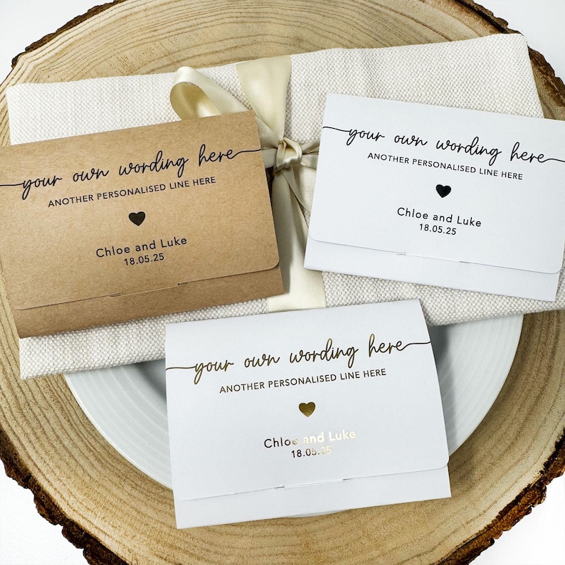 K&ouml;nnte beinhalten: Drei personalisierte Karten mit dem Text "your own wording here" und "ANOTHER PERSONALISED LINE HERE". Jede Karte hat ein Herzsymbol und die Namen "Chloe and Luke" mit dem Datum "18.05.25". Eine Karte ist braun, zwei sind wei&szlig;.