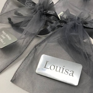 以下が含まれることがあります： 「サラ」と「ルイザ」という名前の入った銀色のギフトタグ2枚が、黒いリボンで結ばれたグレーのオーガンザ製のギフトバッグに入っています。タグには、「ハッピーバースデーサラ」と「ラブフロムマムX」という文字が1枚に、「ルイザ」という文字がもう1枚に書かれています。