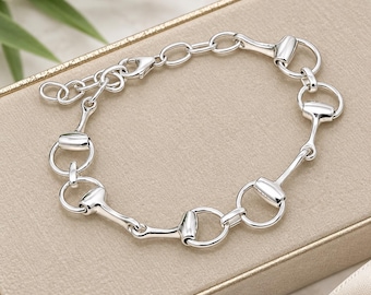 May include: A polished silver chain bracelet featuring a series of repeating equestrian-inspired horse bit links connected by circular rings. The bracelet includes a lobster claw clasp and an adjustable extender chain with small circular links.